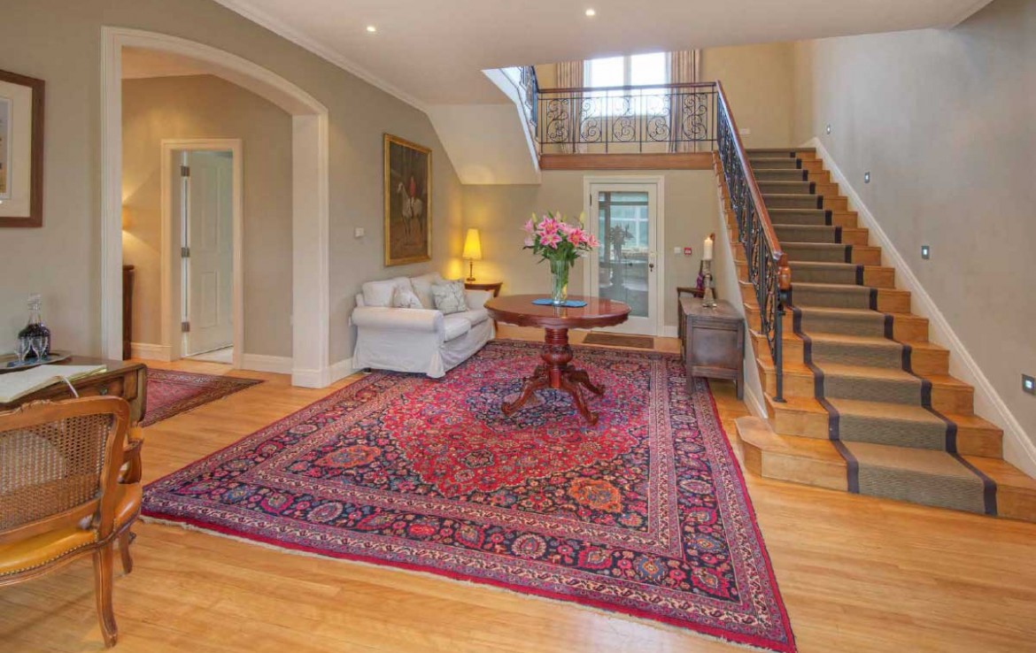 Hall of Dunglass Estate House with persian carpet, oak staircase turning to left and comfortable couch under stairs
